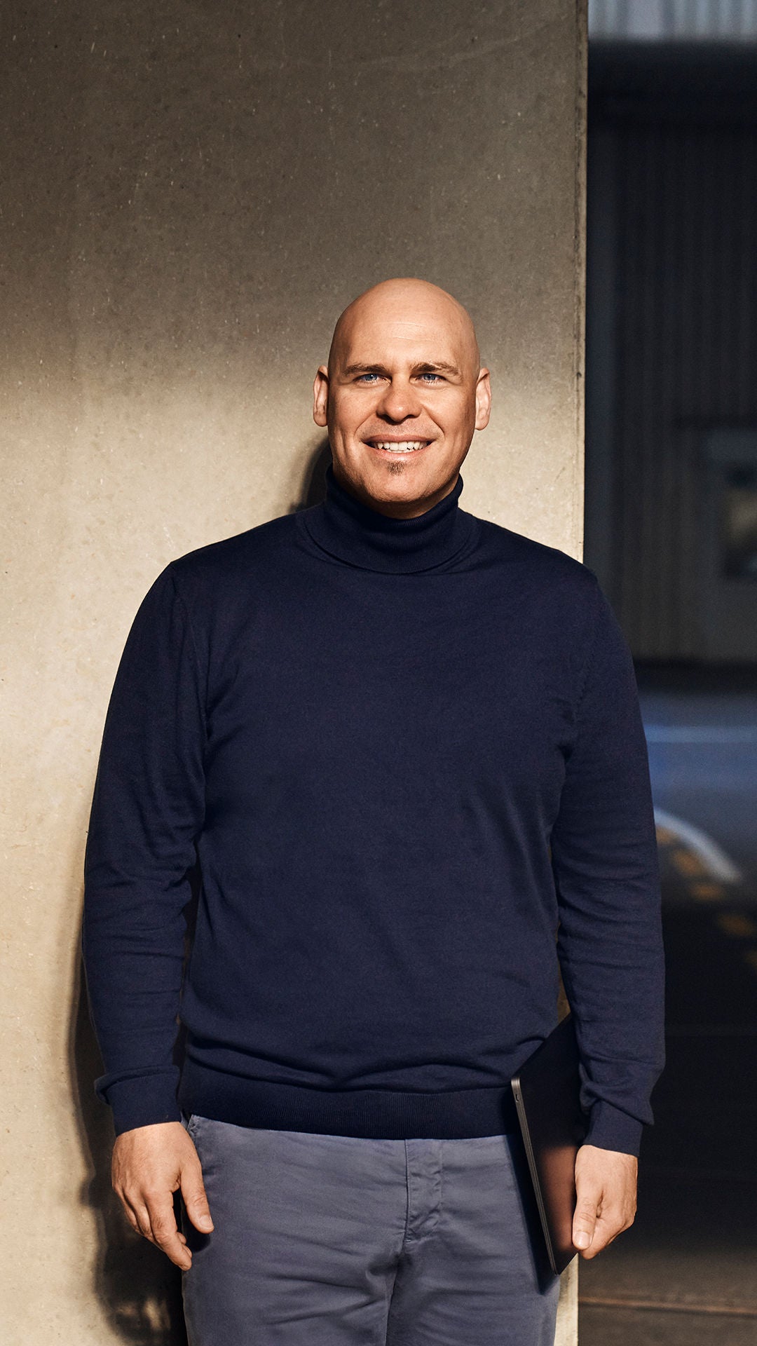 Sebastian schaut an der Kamera vorbei und lächelt. Er steht halb vor einer Wand und einem Audi im dunkeln