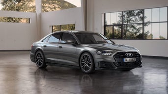 Graue Audi A8 Limousine steht in lichtdurchflutetem Raum mit großen Fenstern und Blick auf bewaldete Hügel.