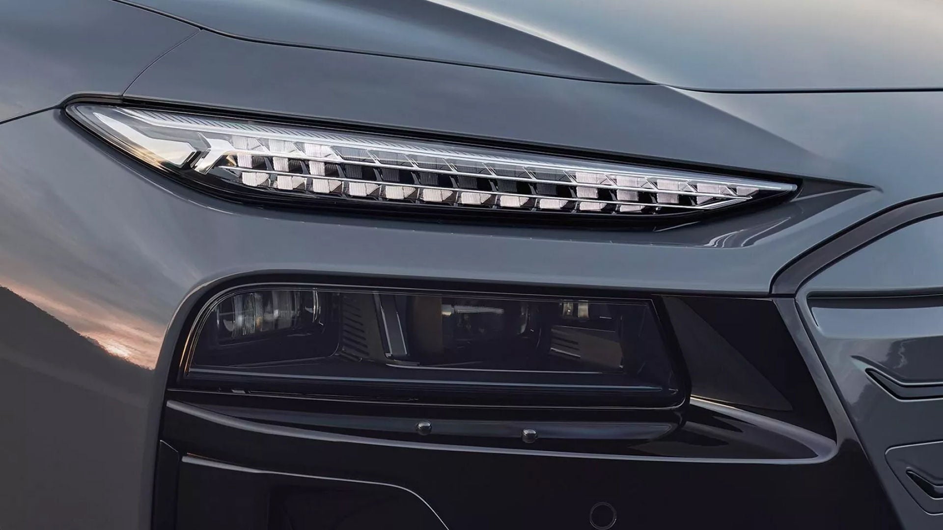 Close-up of a sleek car's front headlight, showcasing bright LED strips and a modern, aerodynamic design in a metallic grey finish.