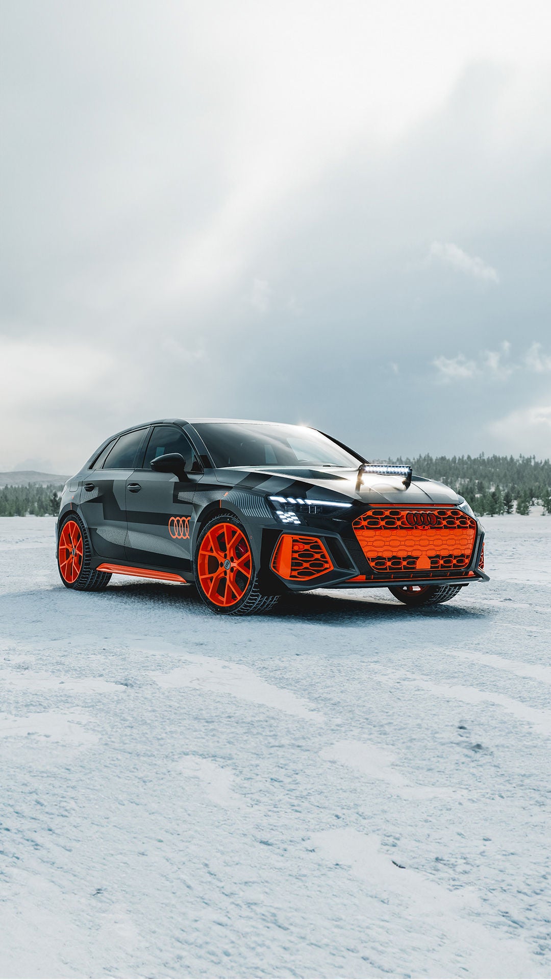 Schwarzer Audi RS 3 driving experience mit auffälligen orangeroten Felgen und Details steht auf schneebedeckter Fläche vor bewaldetem Hintergrund.