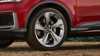 Nahaufnahme eines vorderen Leichtmetallrads mit 5-Speichen-Design an einem roten Audi SUV auf trockenem, erdigem Untergrund.