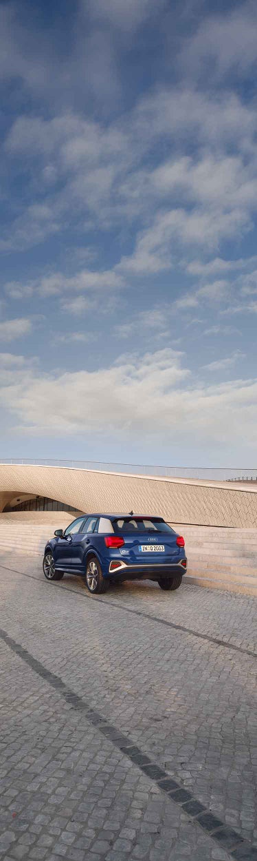 Ein blauer Audi Q2 von hinten auf Platz vor modernem Gebäude.