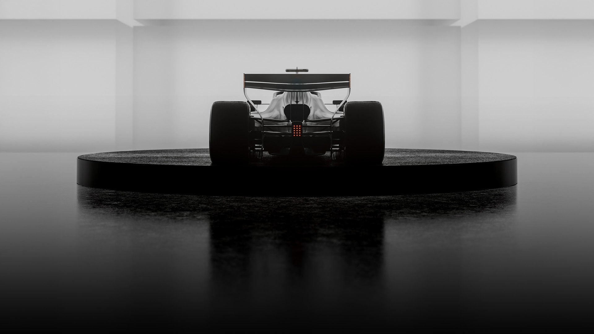 Rückansicht eines Formel-Rennwagens auf einer dunklen, minimalistischen Bühne mit breiten Reifen und beleuchtetem Heck.