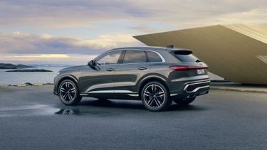 The Q5 SUV is shown in profile in a car park right by the coast. Next to it is a small, futuristic house.