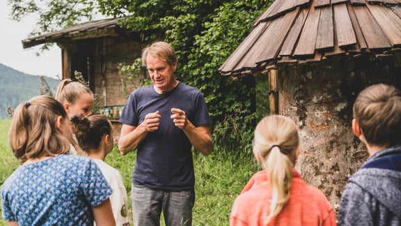 A man stands in front of a group of children and explains something