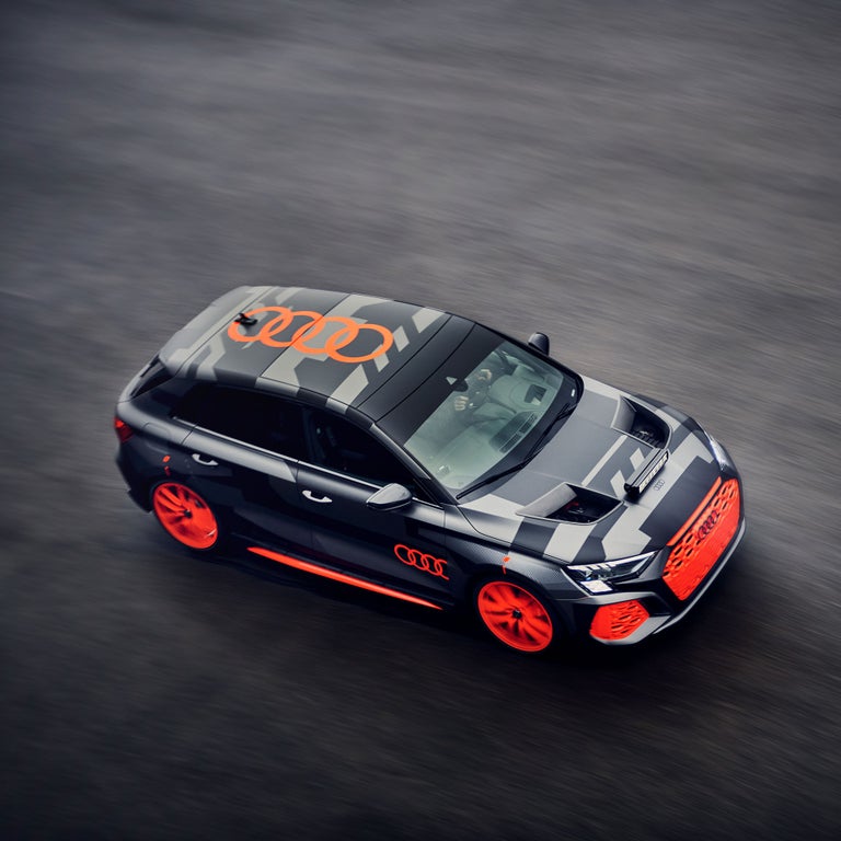 Schwarz/grauer Audi RS 3 driving experience mit orangenen Akzenten fährt auf nasser Straße, Draufsicht mit Bewegungsunschärfe.