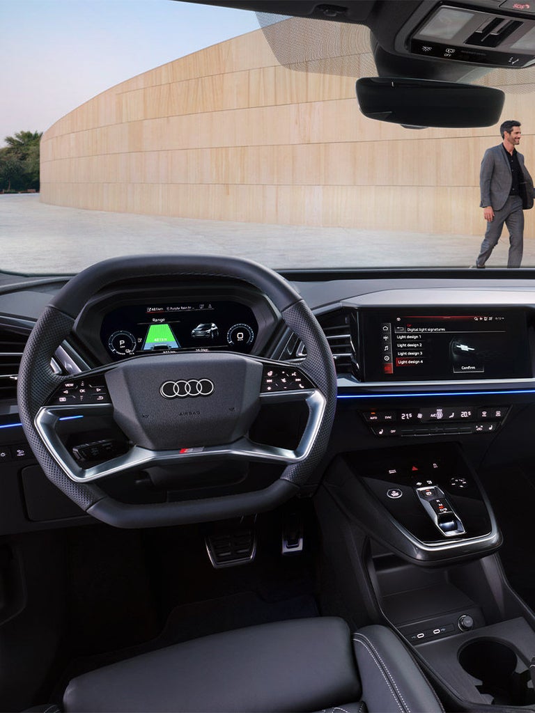 Digitales Cockpit eines Audi Q4 e-tron mit Multifunktionslenkrad, Fahranzeigen und Touchscreen zur Lichtsignatur-Auswahl.