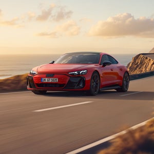 Der e-tron GT quattro auf einer kurvigen Küstenstraße bei Sonnenschein, zur Linken das Meer, zur Rechten felsiges Gebirge.