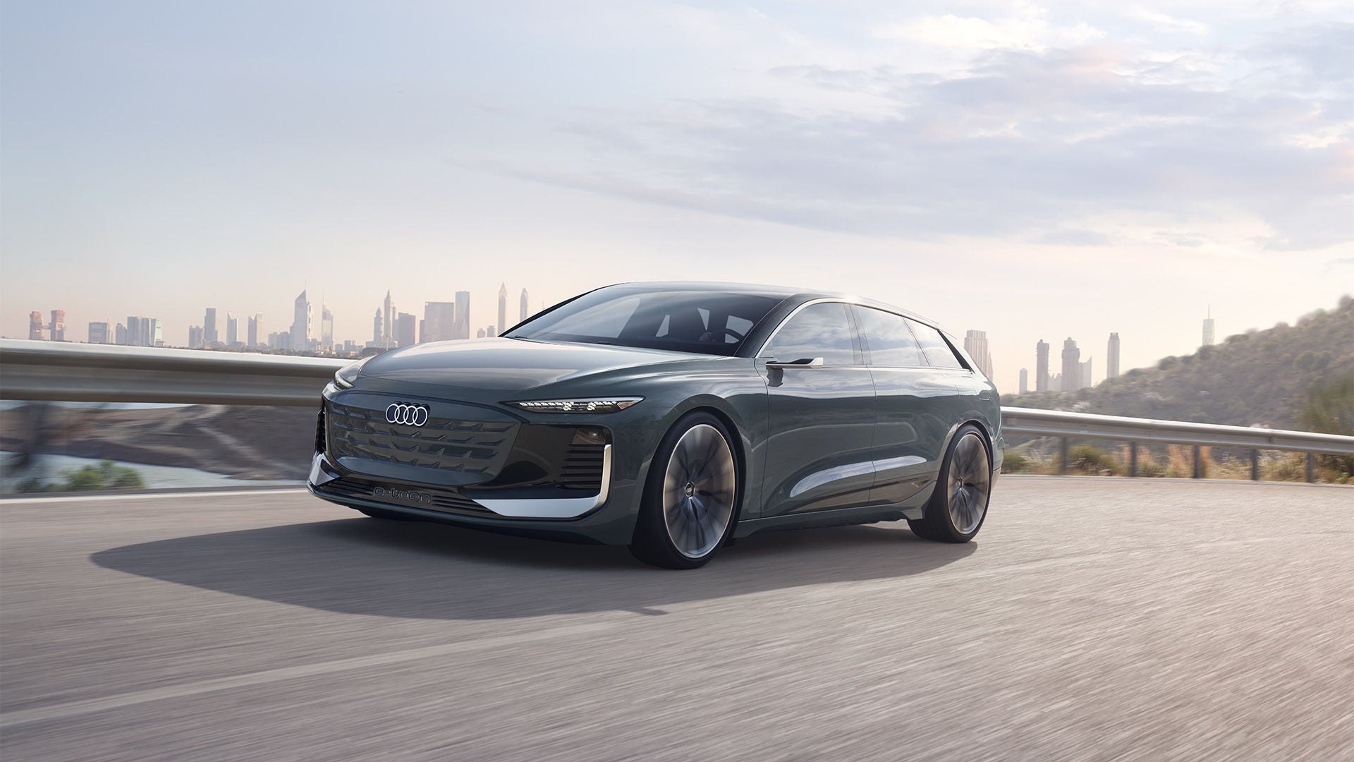 Dunkelgrüner Audi Konzeptwagen fährt auf leerer Straße mit Skyline im Hintergrund bei Sonnenaufgang.