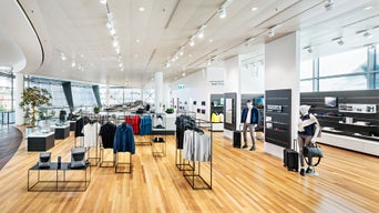Heller Audi Shop mit Holzfußboden, Kleidung und Accessoires auf Displays sowie Schaufensterfront mit Tageslicht.