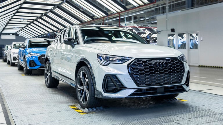 Weiße und blaue Audi Q3 Fahrzeuge in heller Endkontrollstation mit reflektierenden Lichtpaneelen.