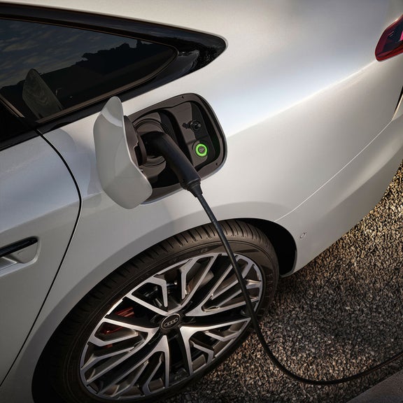A close-up of an electric car charging port, with a charging cable connected and a green indicator light visible.  