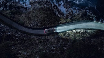 Ein Audi von oben mit eingeschaltetem Licht fährt nachts auf kurviger Straße durch felsige Landschaft.