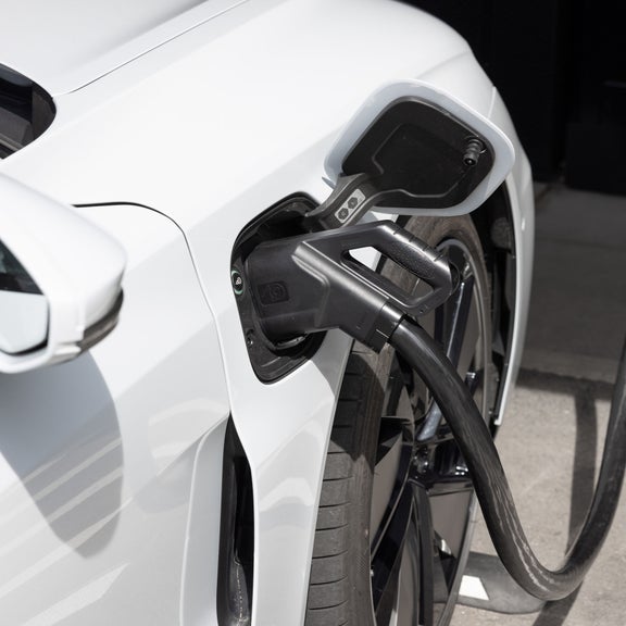 Ein weißes Elektroauto wird an der vorderen rechten Seite über ein Ladekabel an einer Ladesäule aufgeladen.