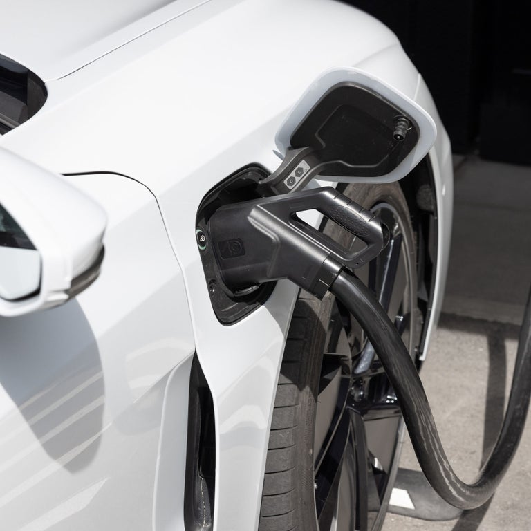 Ein weißes Elektroauto wird an der vorderen rechten Seite über ein Ladekabel an einer Ladesäule aufgeladen.