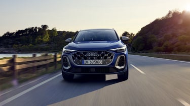 Frontprofil des SQ5 SUV in dunkelblau, welcher auf einer Straße durch die Natur fährt. Am Steuer sitzt eine junge Frau.