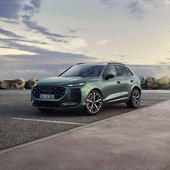 A green Q3 SUV is parked near a coastal area with rocks in the background under a cloudy sky, conveying a modern and adventurous tone.