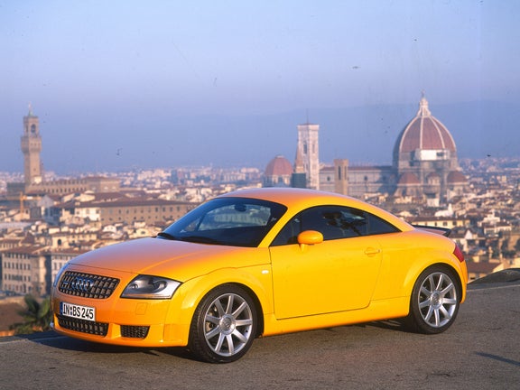 A yellow Audi TT Coupé 3.2 quattro in front of a city backdrop