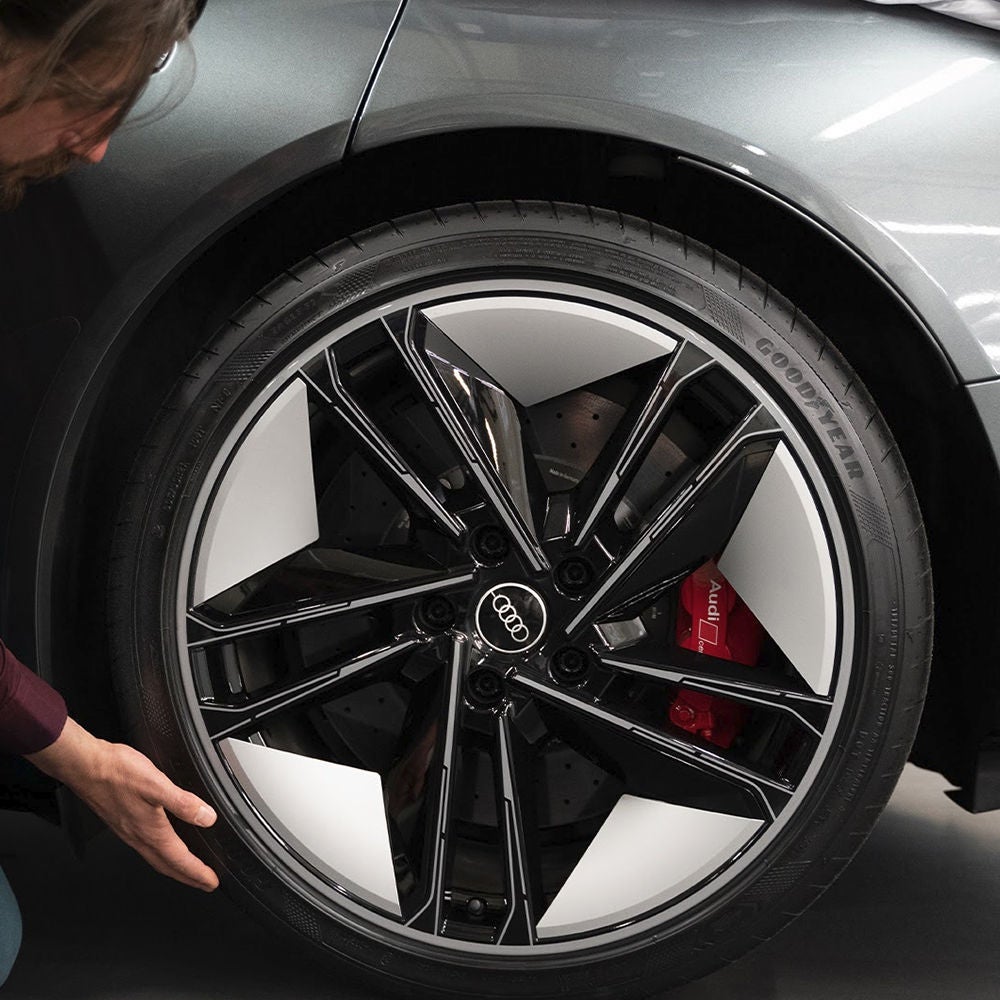 A man stands next to an Audi RS Q8 and gazes into the distance. A skyline can be seen on the horizon.