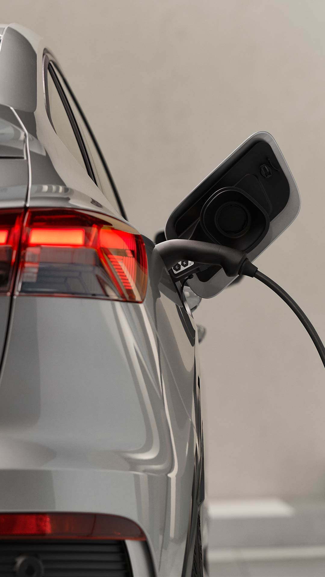 Nahaufnahme des Ladesteckers eines silbernen Audi Q4 Sportback e-tron mit leuchtendem Rücklicht, im Hintergrund ist verschwommen ein Mann in Anzug.