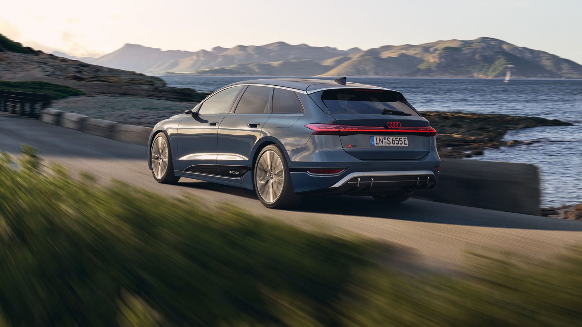 A blue Audi S6 Avant e-tron in motion on a coastal road