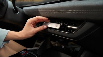 Hand steckt Audi-Duftspender in Lüftungsgitter im Auto-Innenraum.