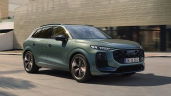 A green Audi Q3 driving on a city street, showcasing a sleek design with modern headlights and a prominent grille. The tone is dynamic and urban.