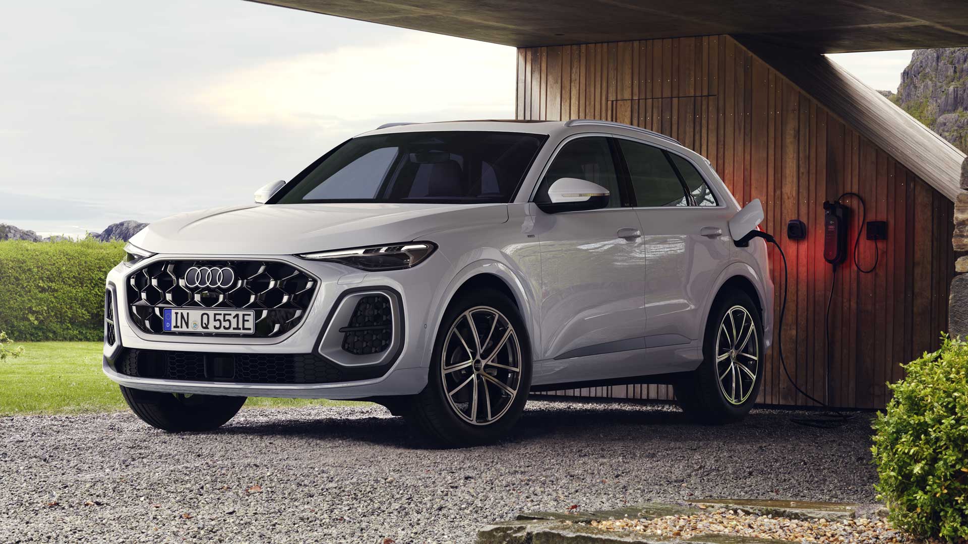 Ein weißer Q5 SUV e-hybrid in schräger Frontansicht ist unter einem Carport an eine Ladestation angeschlossen.
