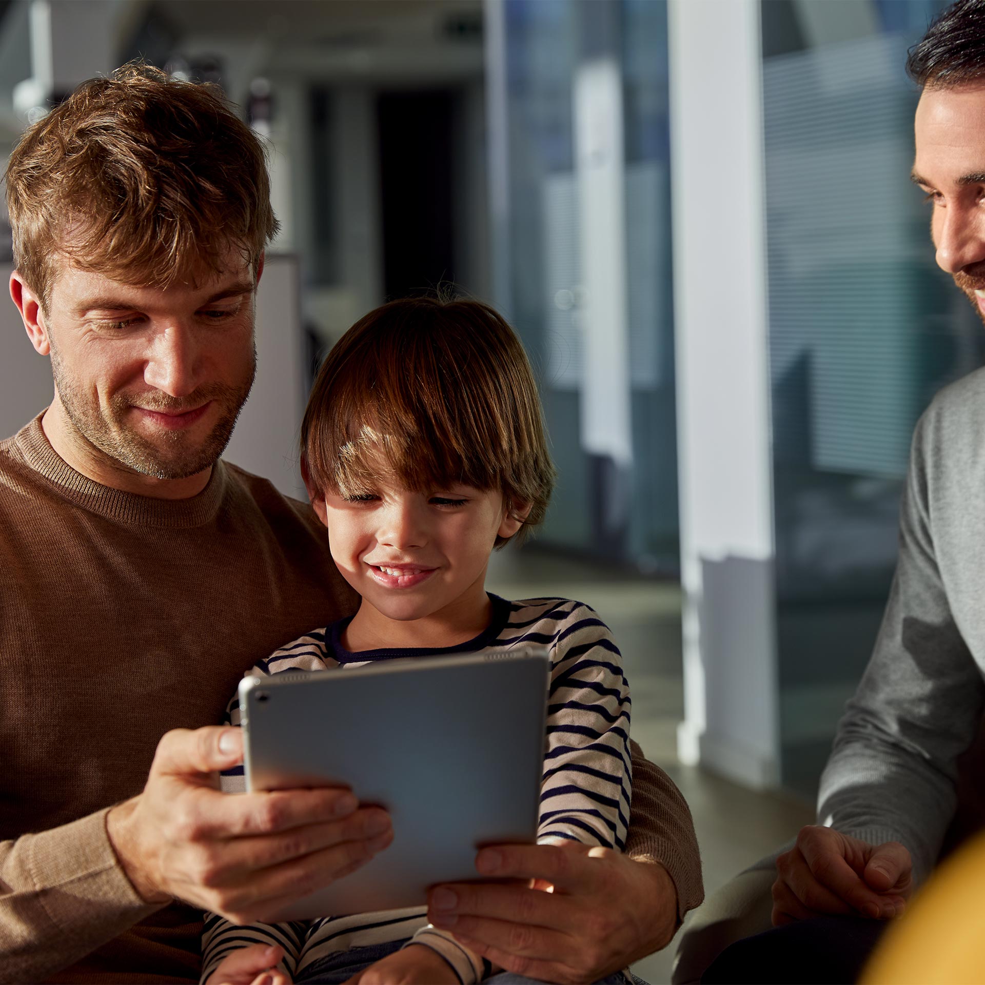 A man and a child use a tablet computer in an Audi showroom while a salesman watches.