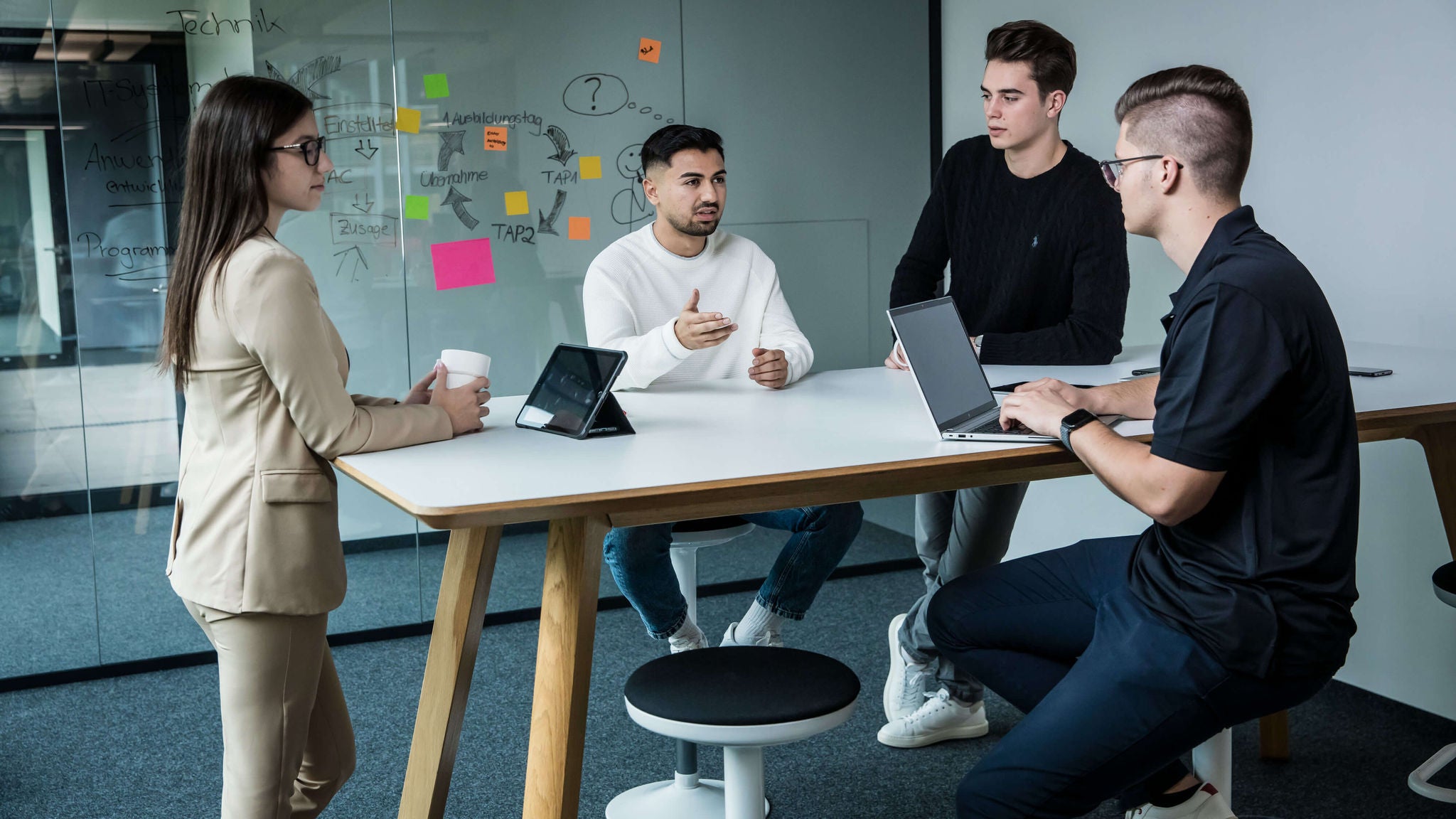 Gruppe junger Menschen im Gespräch an einem Tisch mit Laptops im Besprechungsraum.