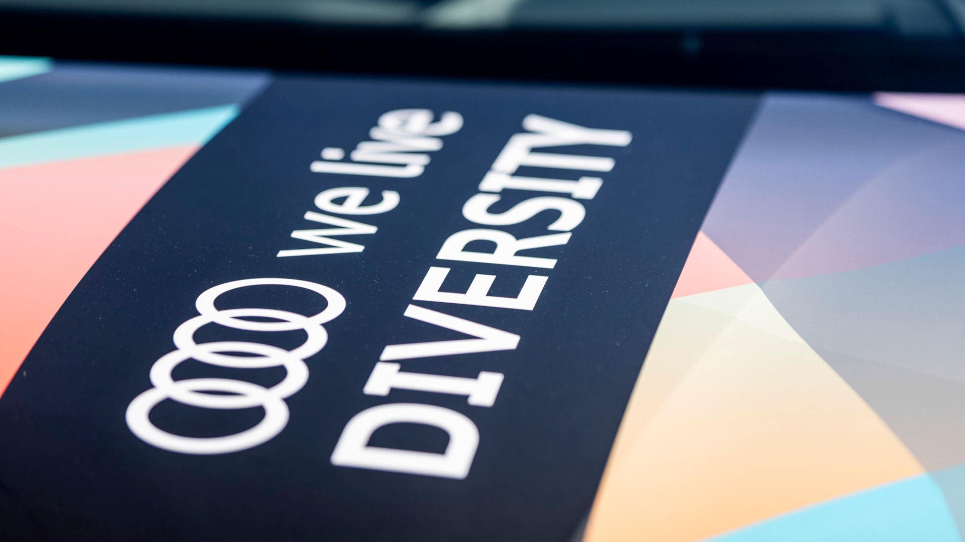 Audi mit bunter Audi-Beklebung und Schriftzug 'we live diversity' auf dem Parkplatz.