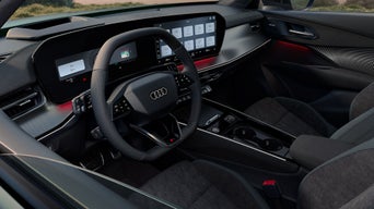 Innenraum eines Audi Modells mit schwarzem Lenkrad, großem Digitaldisplay und Ambiente-Beleuchtung in Rot.