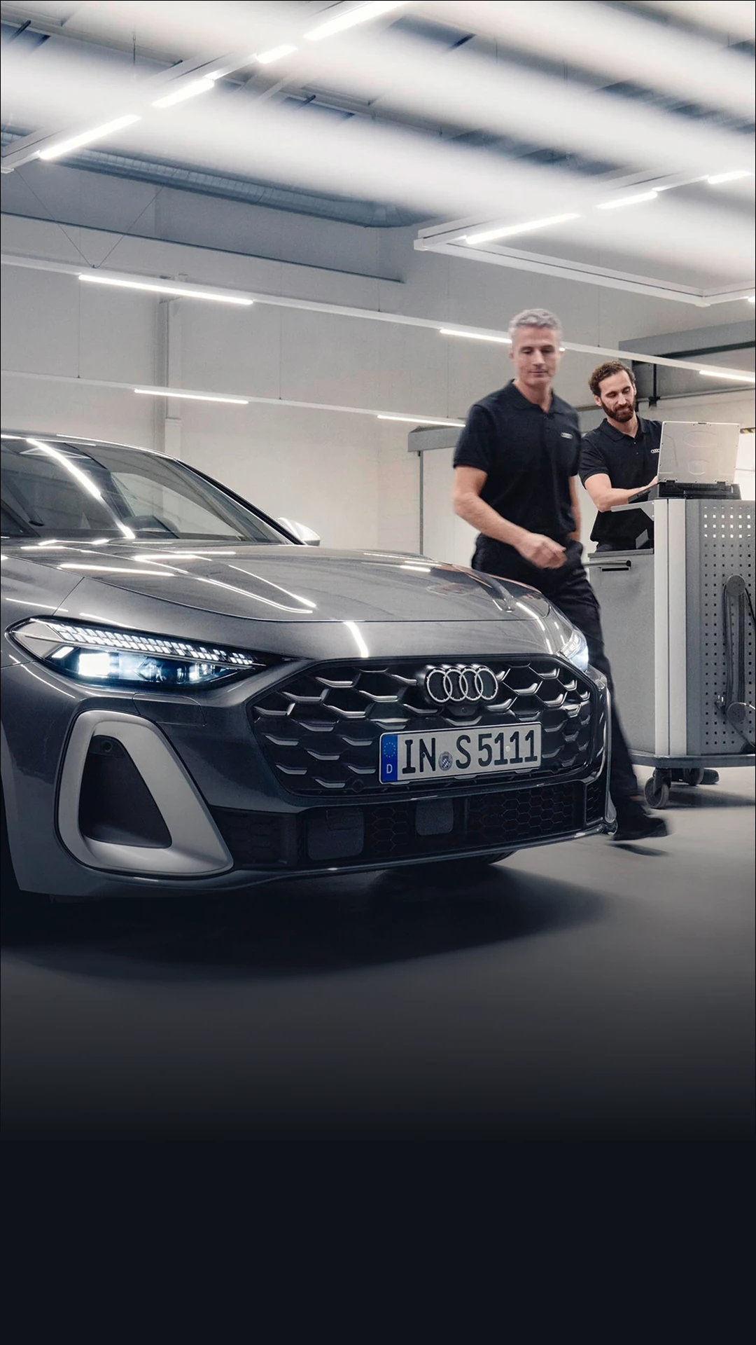 Audi vehicle in a workshop alongside technicians and diagnostic equipment during a repair and maintenance service.