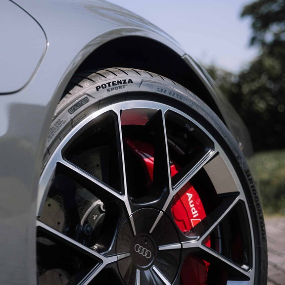 Nahaufnahme eines Audi-Rades mit schwarzer und silberner Felge, roter Bremssattel mit Audi-Logo und Bridgestone Potenza Sportreifen.