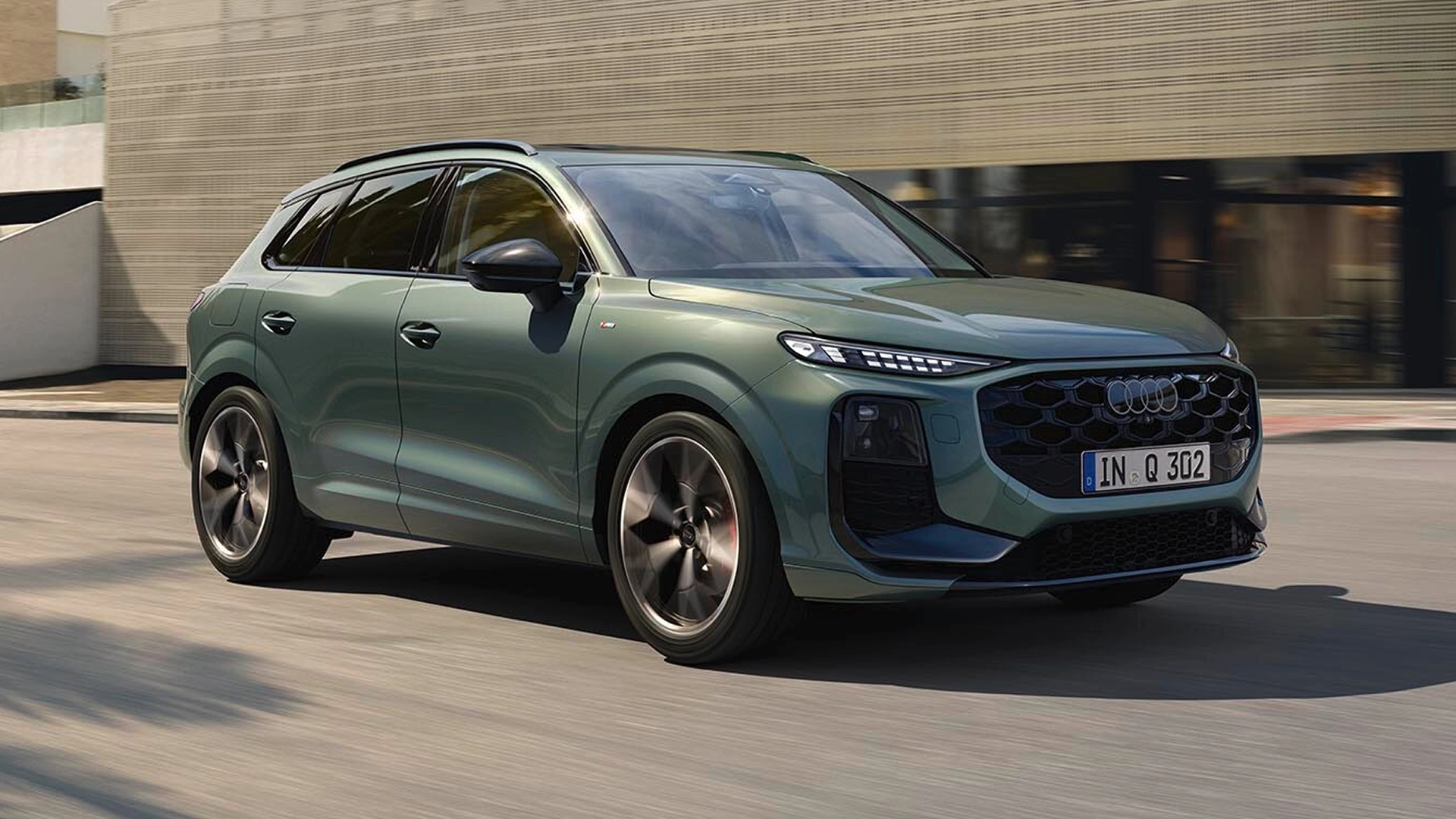 A blue Audi Q3 SUV driving on road, with a building in the background.