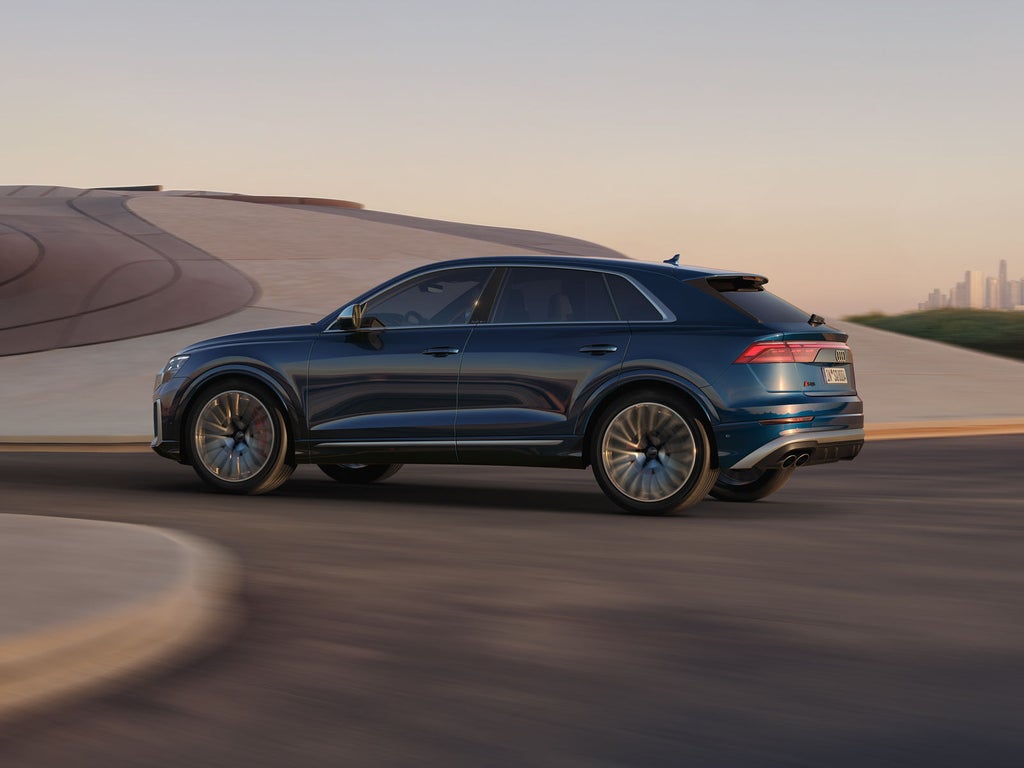 Der SQ8 SUV in Seitenansicht passiert ein futuristisches Gebäude.