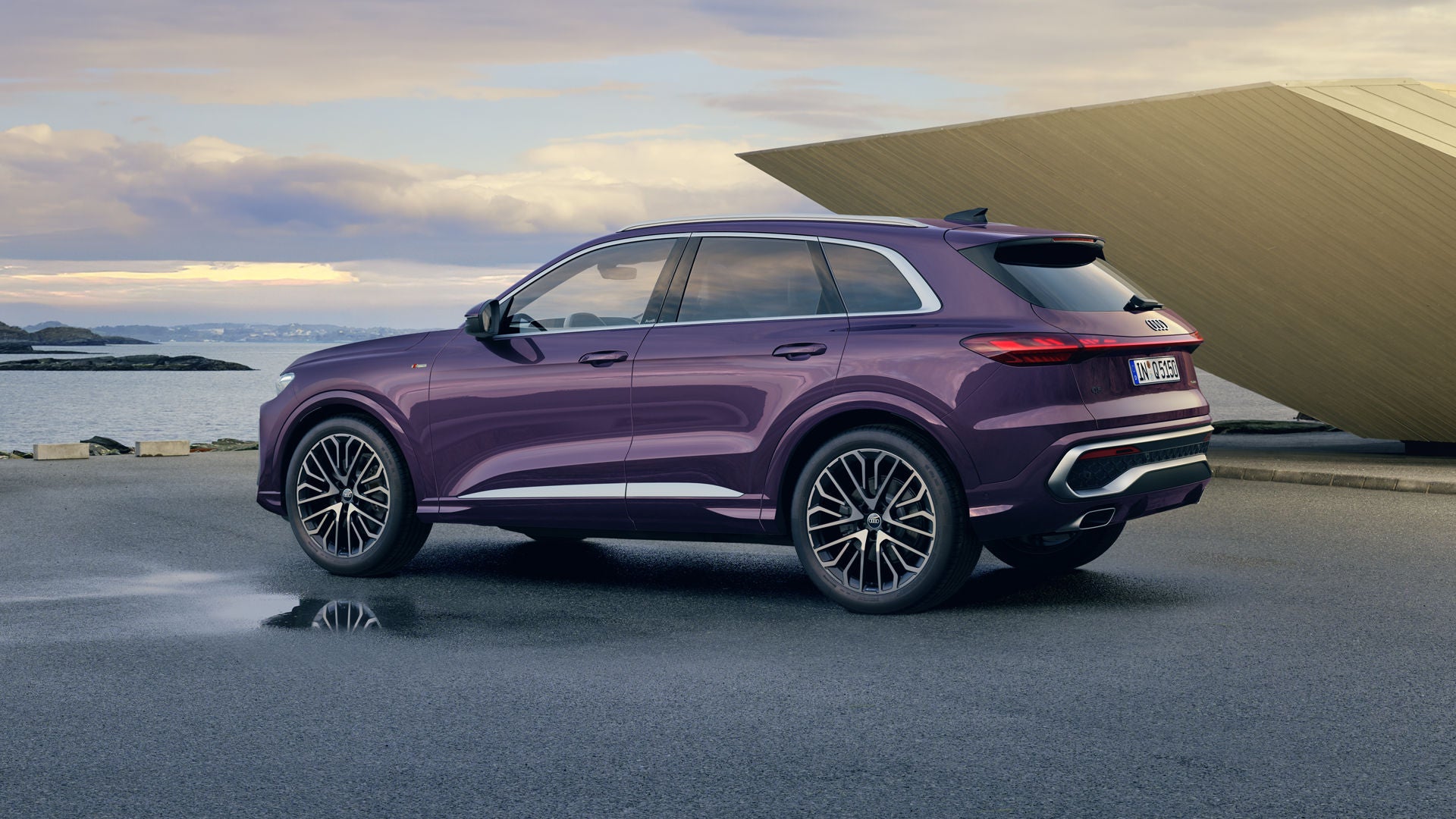 Der Q5 SUV mit der Individuallackierung Merlin Perleffekt steht im schrägen Seitenprofil an der Küste. Rechts von ihm befindet sich ein futuristisches Gebäude.