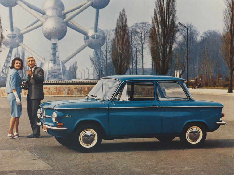 Colour photograph of a couple in front of the Atomium in Brussels next to a blue NSU Prinz