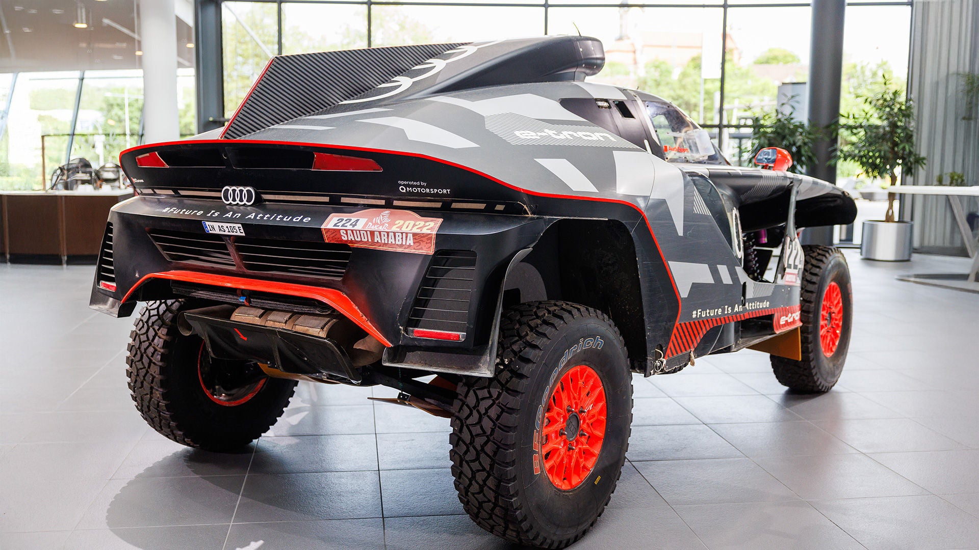 Audi e-tron Rallyeauto mit Offroad-Bereifung und Dakar-Beklebung steht in einer hellen Ausstellungshalle auf grauem Boden.