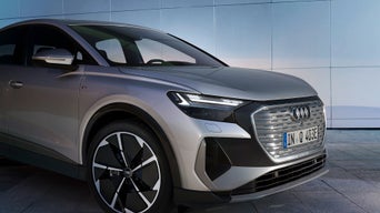 A silver Audi Q4 Sportback e-tron with striking LED headlights, featuring a modern grille and stylish black alloy wheels against a minimalist backdrop.