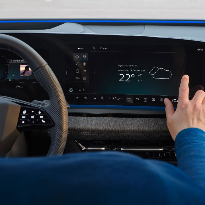 A person touches a sleek car dashboard display showing weather information for Ingolstadt, Germany, with a temperature of 22°C.