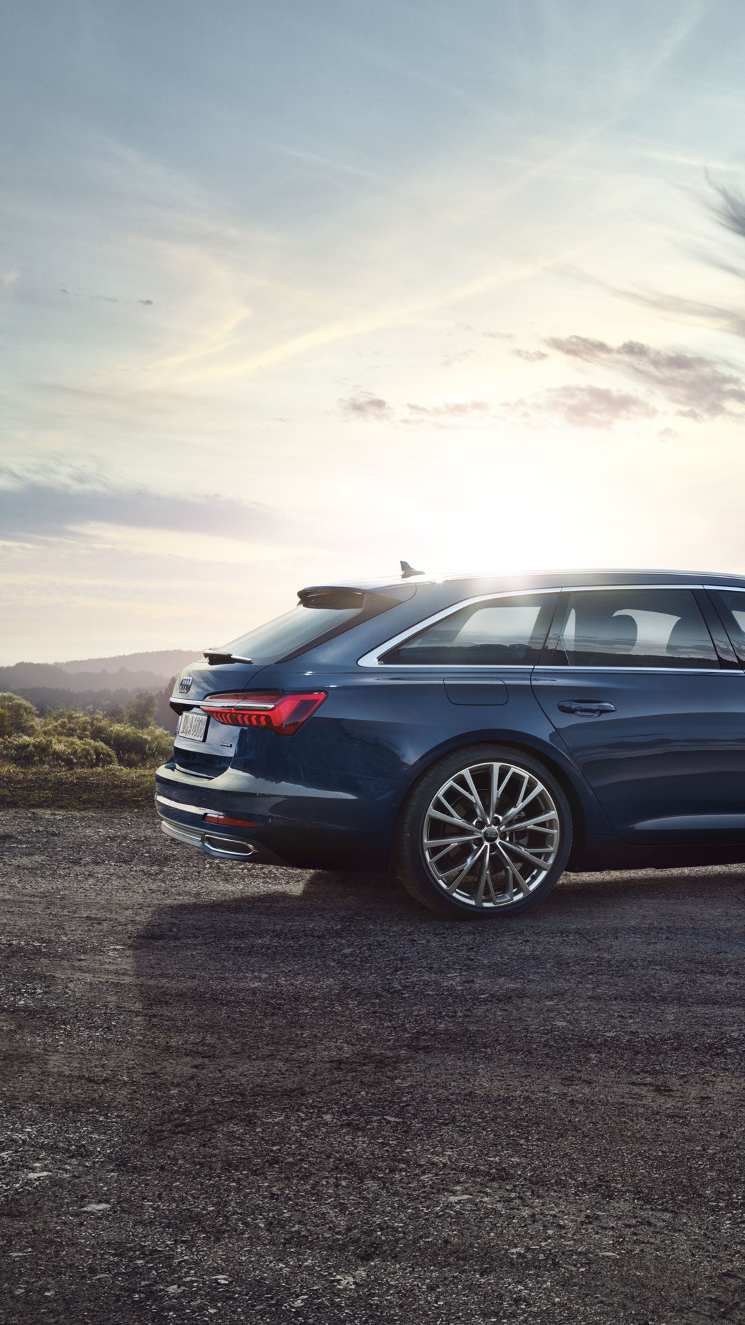 Seitliche Ansicht eines dunkelblauen Audi A6 Avant auf einem Hügel bei Sonnenuntergang mit Blick auf hügelige Landschaft.