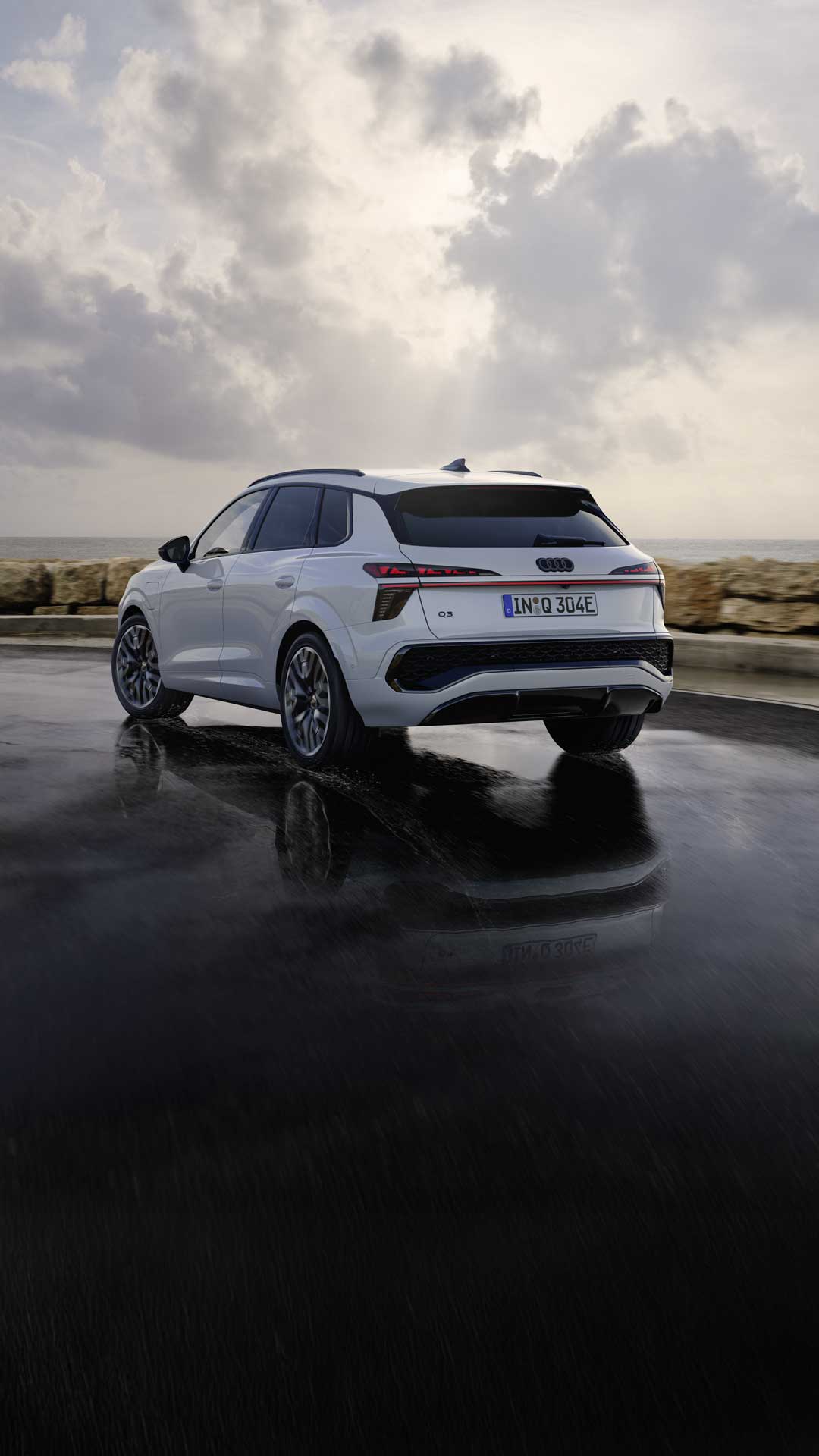A white Q3 SUV e-hybrid drives along a wet road along the coast.