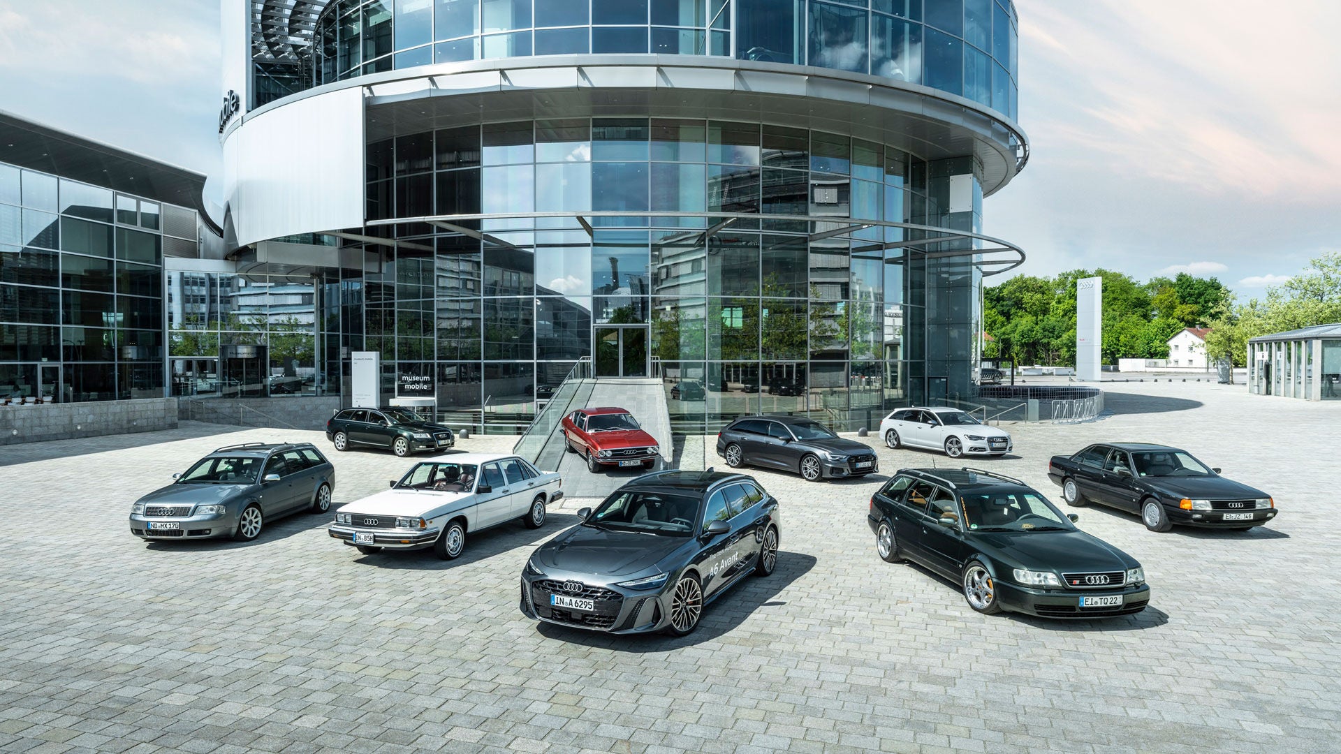 Audi C-series models are lined up in a star shape in front of the round glass front of the Audi museum mobile.