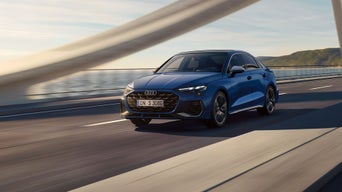Blaue Audi S3 Limousine fährt über eine Küstenbrücke bei Tageslicht.