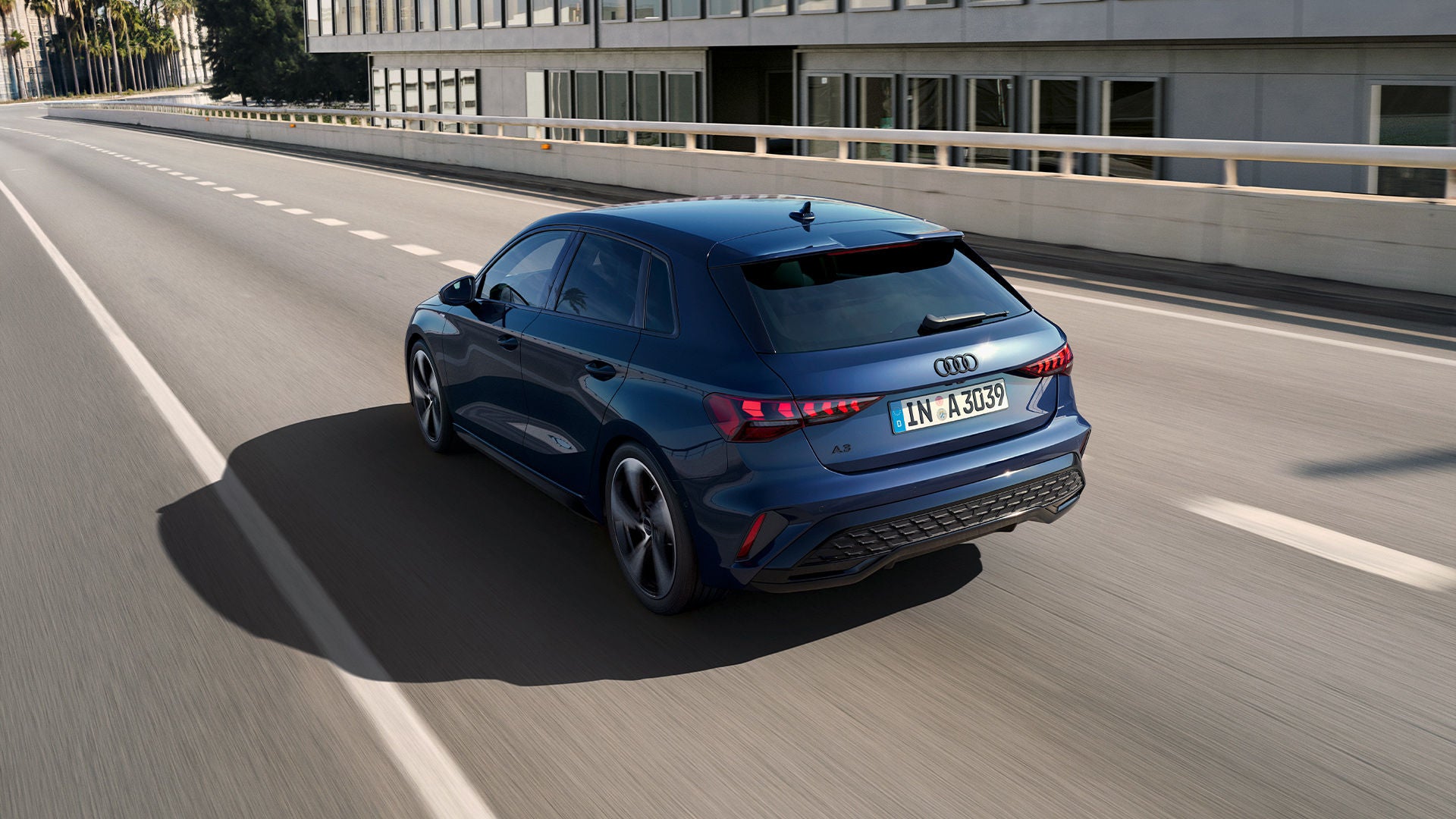 Une Audi A3 bleue roule sur une route urbaine surélevée.