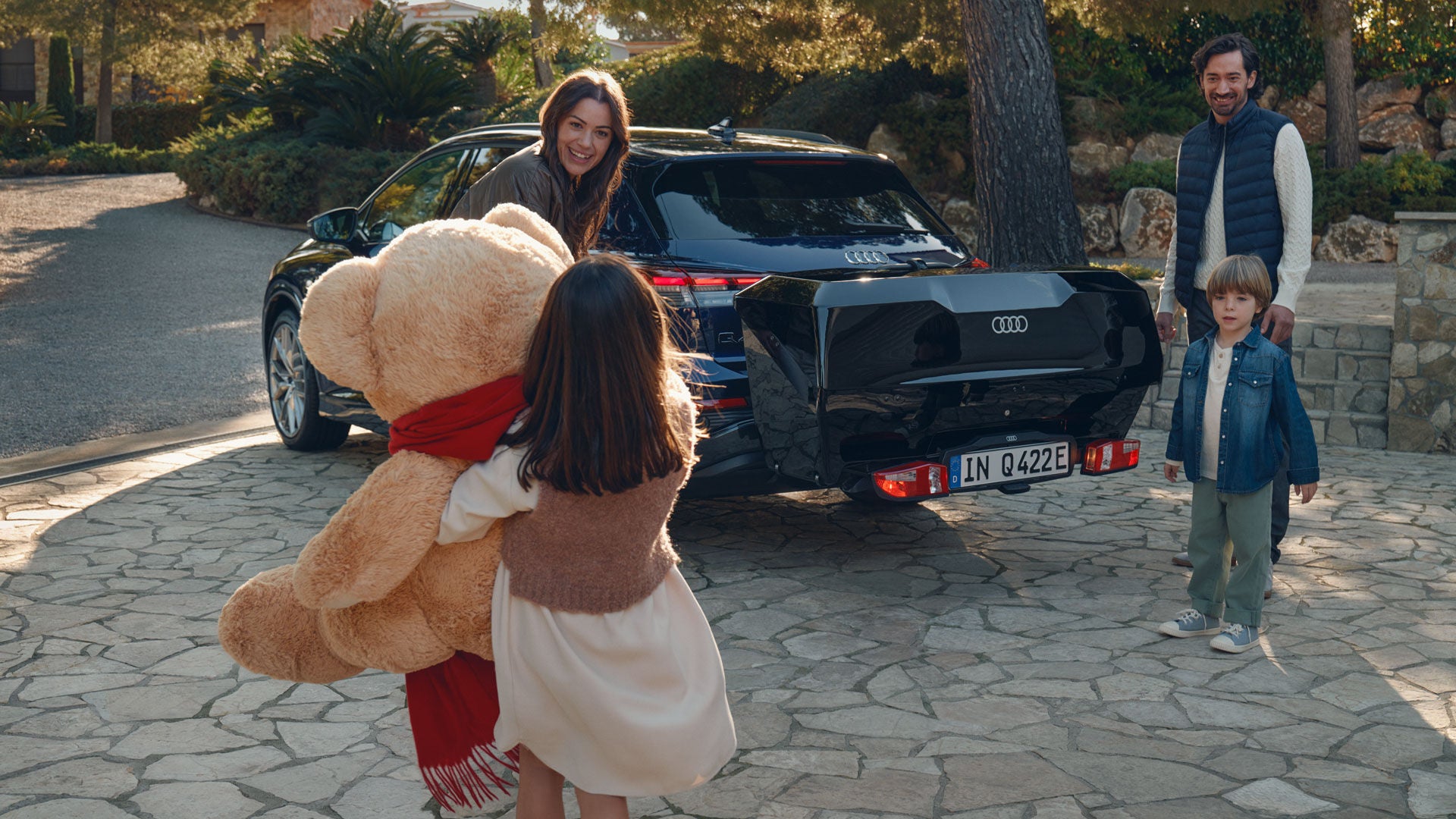 Familie steht am Audi Q4 e-tron mit Heckbox, ein Mädchen hält einen großen Teddybär in den Armen.