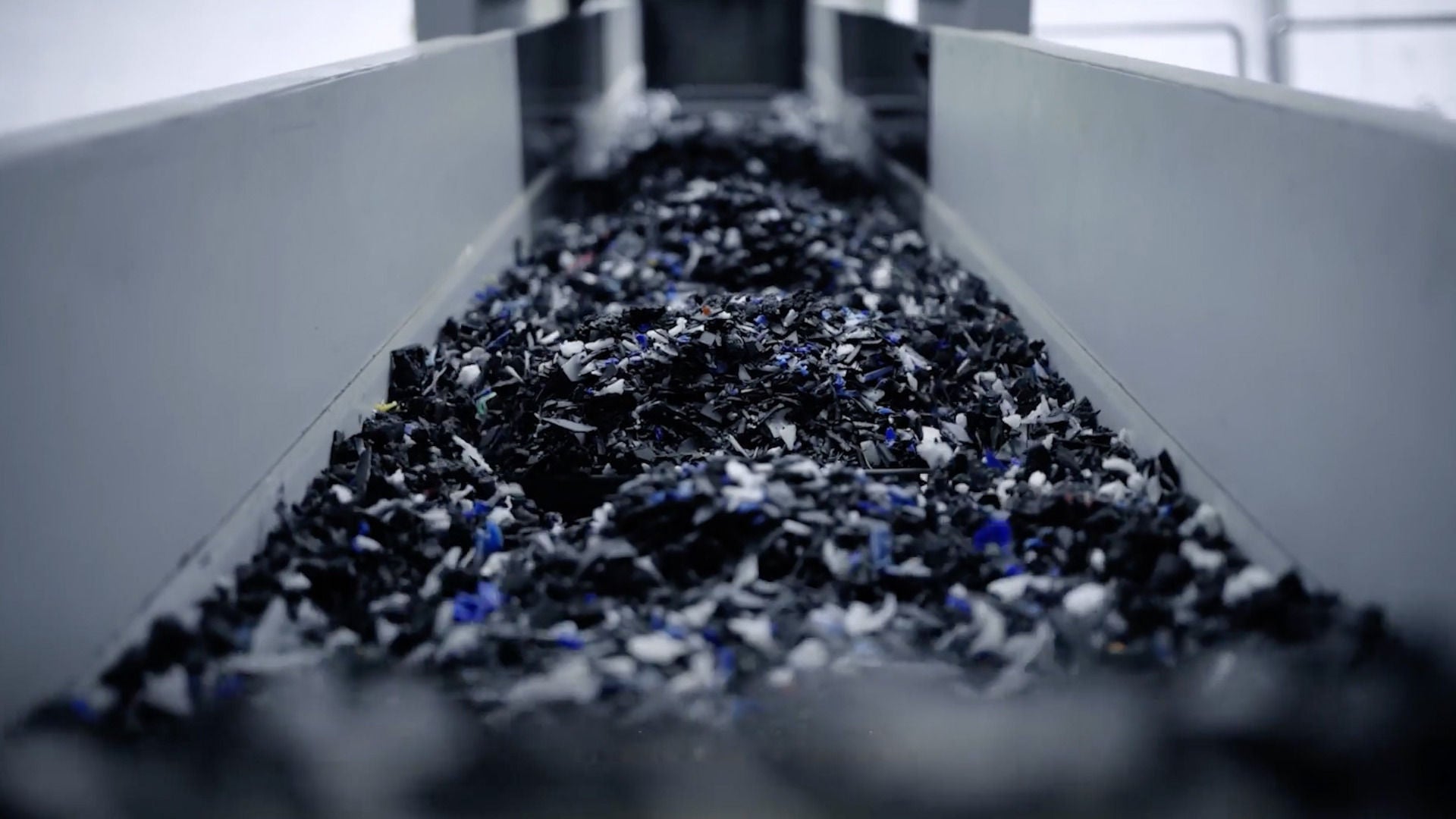 Black and colored pieces of plastic move along a conveyor belt in an industrial environment.