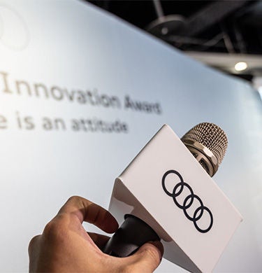 Person holds a microphone with the Audi logo up in the air in front of an Audi poster.