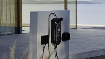 A charging station with cable is attached to the front of a modern house.